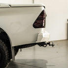 Close-up of a white car's rear with a tow hitch attached, on a light gray floor.